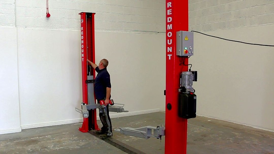 A worker checking the condition of a 2 post car lift